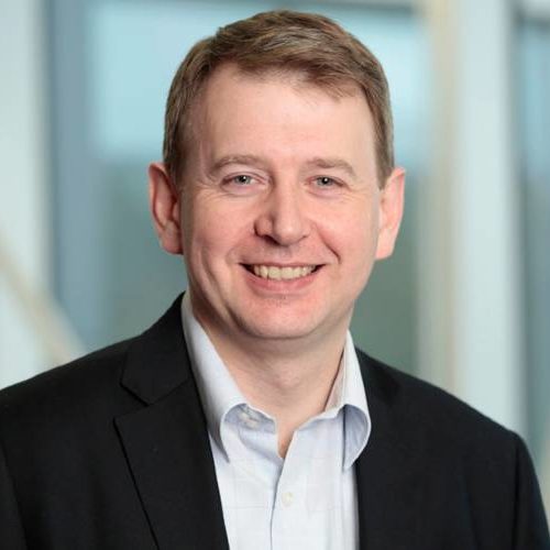 White man with short brown hair and black suit smiles.