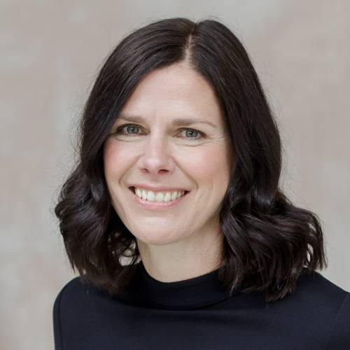 White woman with short brown hair smiles against beige background.